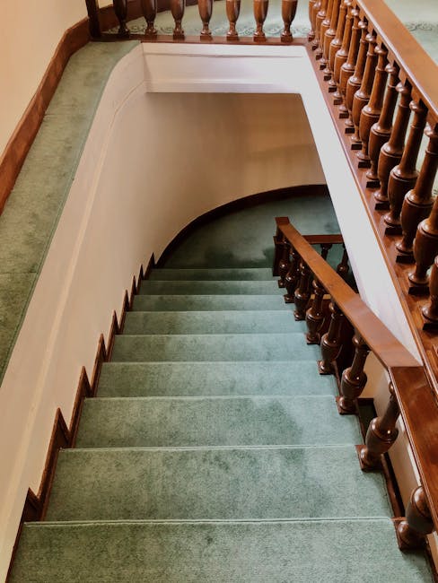 A person wearing dark blue jeans and a blue sneaker is stepping down a carpeted staircase with red and beige colored carpet runners. The staircase is illuminated by natural light from the side, highli